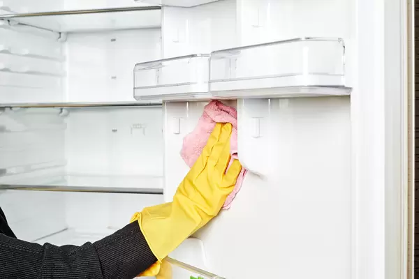 Housewife hands in rubber protective glove with microfiber cloth cleaning a fridge