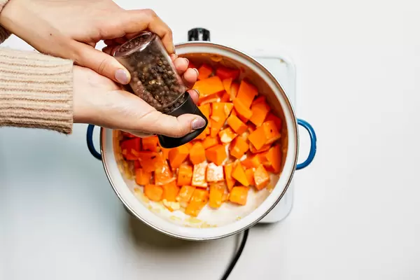 Housewife pouring peppercorns on food