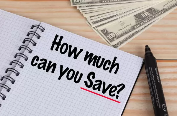 How much can you Save text in notebook and Dollar banknotes on wooden table