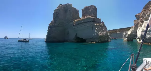 Huge rock formation and sail boats on the blue cretan sea, in a bay of Milos, Greece