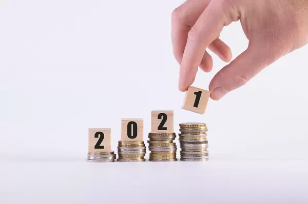 Human hand and stack of coins with wooden cubes with 2021 text