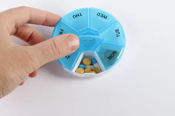 Human hand with plastic pill box on white background