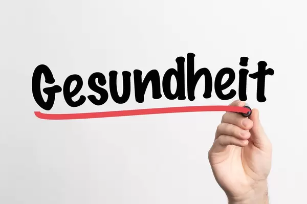 Human hand writing Gesundheit on whiteboard