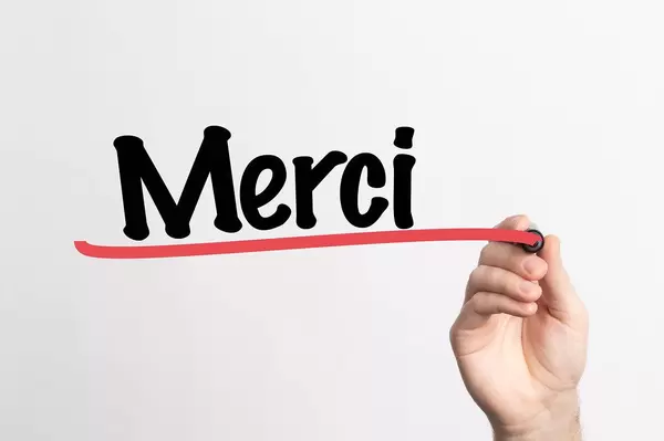 Human hand writing Merci on whiteboard