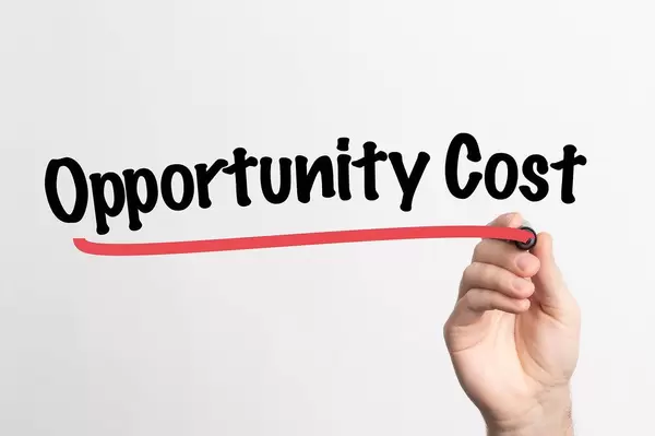 Human hand writing Opportunity Cost on whiteboard