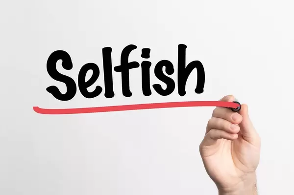 Human hand writing Selfish on whiteboard