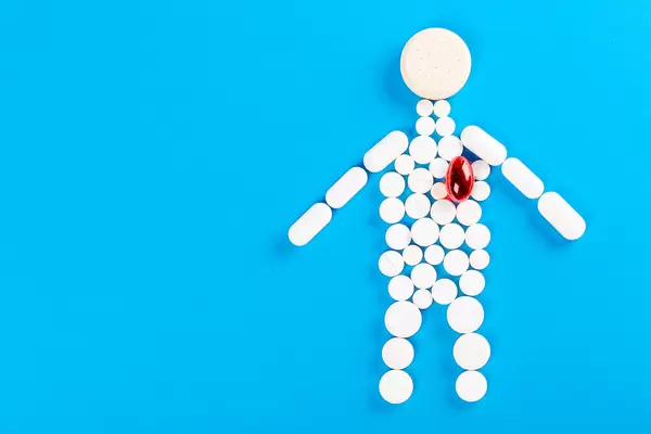 Human made of white tablets on a blue background with a red capsule instead of a heart