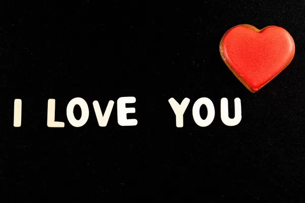 I love you - made of wooden letters on a black background with a gingerbread heart