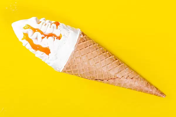 Ice cream in sweet waffle cone with caramel topping in yellow background