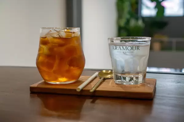 Iced Oolong Green Tea with Mango, Paper Straw, Spoon and a Glass of Iced Water on a Wooden Board in a Cafe
