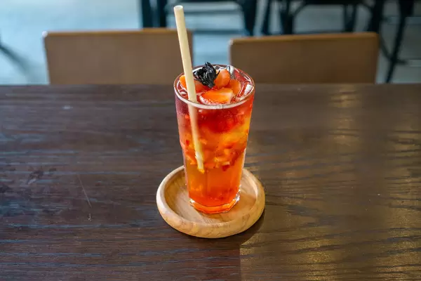Iced Strawberry Oolong Tea with Strawberry and Dried Hibiscus as Topping on a Wooden Saucer with Paper Straw