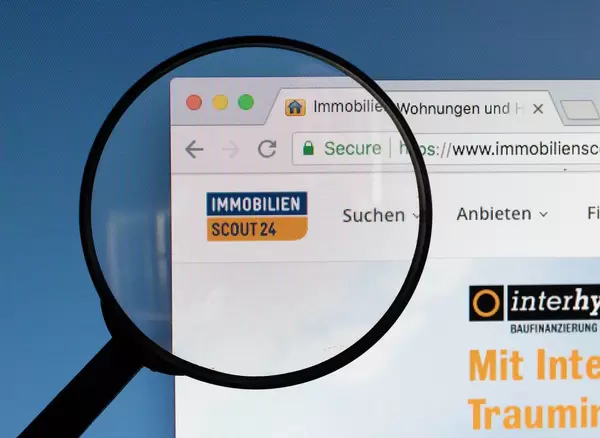 Immobilien Scout 24 Logo am PC-Monitor, durch eine Lupe fotografiert