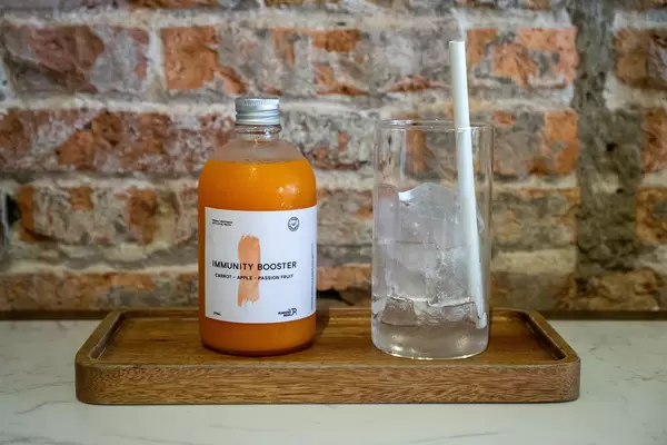 Immunity Booster Fresh Juice with Pressed Carrot, Apple and Passion Fruit in a Glass Bottle next to a Drinking Glass with Ice Cubes and Paper Straw