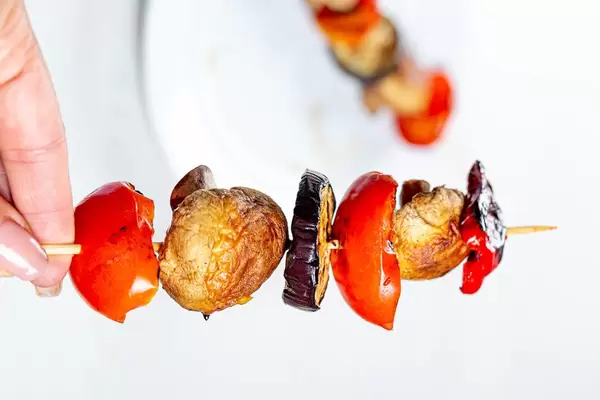 In a woman's hand a small wooden skewer with grilled vegetables