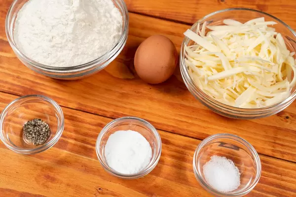 In Glasschalen abgewogene Zutaten zum Kochen und ein Ei auf einem Holztisch