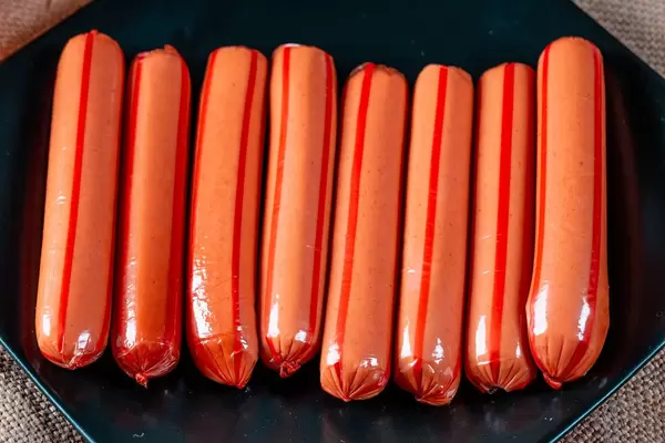 In Plastikfolie eingepackte Würste auf schwarzem Teller