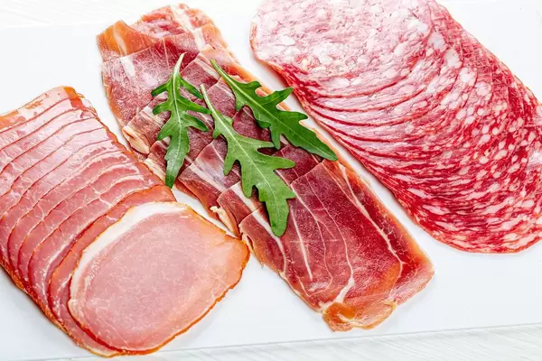 In Scheiben geschnitteter, rockengehärteter Schinken und Salami mit frischer Rucola auf einem weißen Schneidebrett