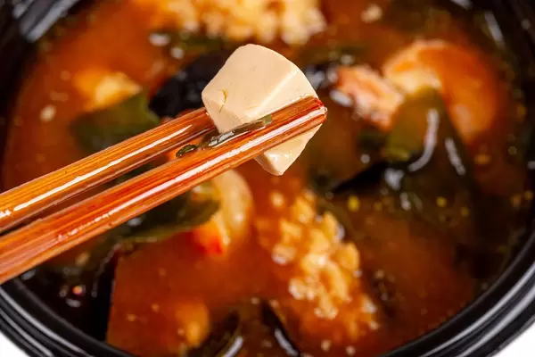 In wooden chopsticks a cube of tofu cheese on the background of miso soup