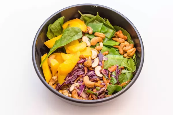 Indian Summer Bowl mit Blattspinat, Zuckerschoten, warme Rosmarin Kartoffeln, Rohkostsalat, geröstete gelbe Karotten, Cashews, Basilikum, Koriander sowie gelbe Thai-Curry Sauce