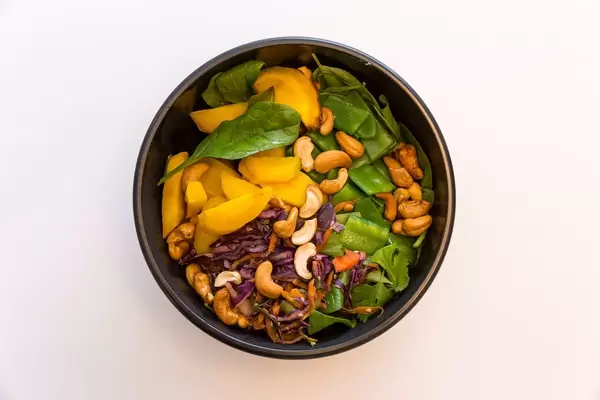 Indian Summer Bowl Top view mit Blattspinat, Zuckerschoten, warme Rosmarin Kartoffeln, Rohkostsalat, geröstete gelbe Karotten, Cashews, Basilikum, Koriander sowie gelbe Thai-Curry Sauce