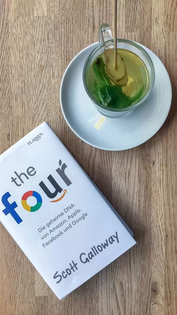 Ingwer-Minz-Tee im Glas, neben der Leselektüre und dem Social-Media-Entschlüsselungsbuch "The Four" von Scott Galloway, auf einem Holztisch