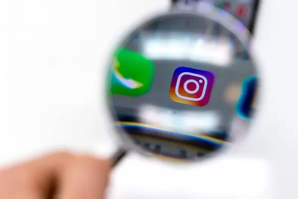 Instagram app on mobile phone photographed through magnifying glass against white background
