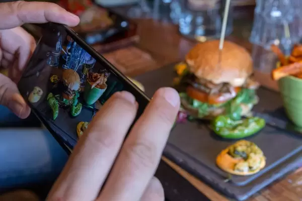 Instagram-Foodblogger fotografiert das Mittagessen: Hamburger mit Pommes-Beilage auf einem schwarzen Tablett auf einem Holztisch im Restaurant