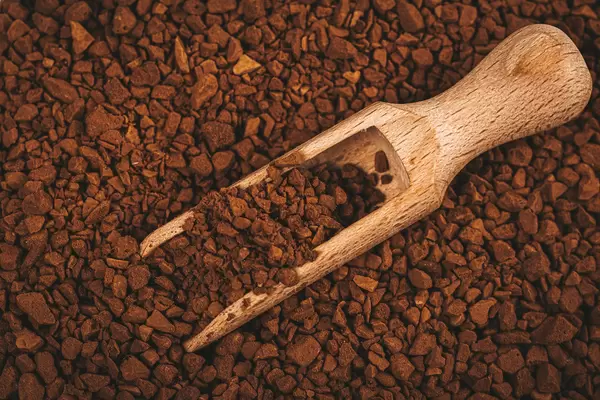 Instant coffee in wooden scoop on coffee granules background