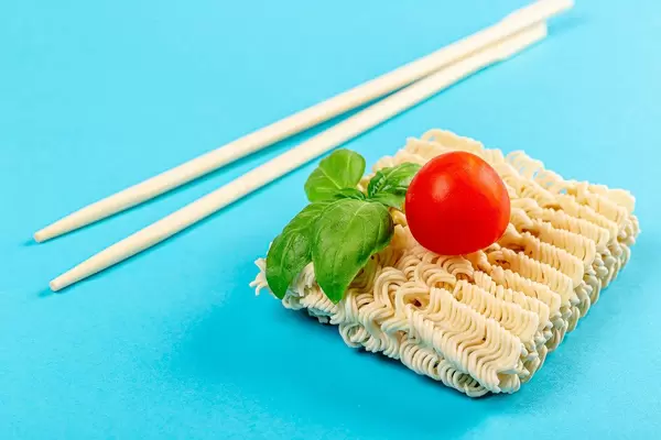 Instant noodles on blue background with chopsticks, basil and tomato