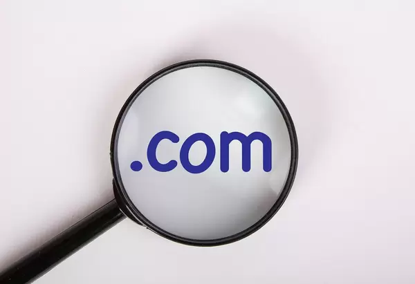 Internationale Domainendung .com in blau auf weiß, vergrößert dargestellt unter einer Lupe