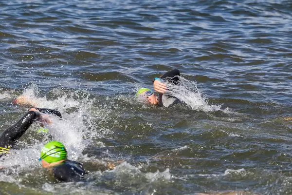 Ironman athletes, with swimming caps and swimming goggles, front crawl in the Finnish lake Vesijärvi in Päijät-Häme
