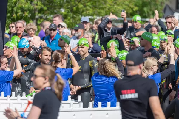 Ironman-Teilnehmer in Neoprenanzügen und Badekappen, werden im finnischen Lahti vor dem Schwimmwettkampf angefeuert