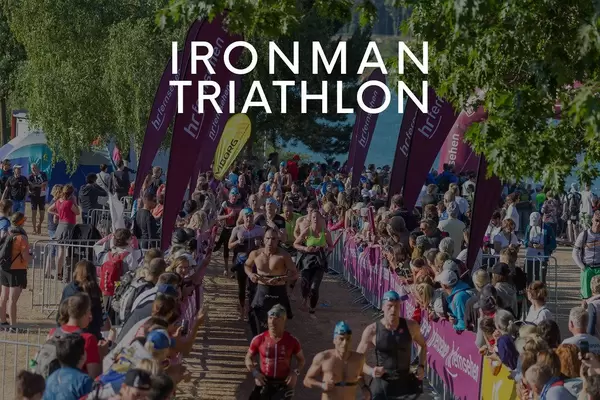 Ironman Triathlon participants in swimsuits with swimming caps, run between spectators