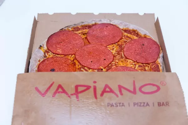 Italian-style restaurant chain Vapiano's new vegan salami pizza in a cardboard take-away packaging on white background