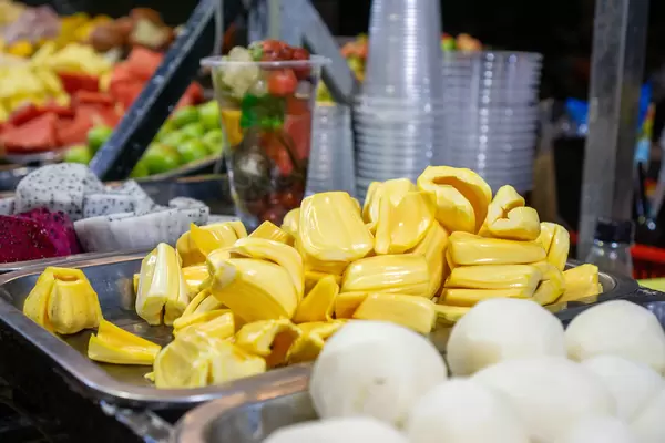 Jackfrucht, Rote und Weiße Drachenfrucht und andere Früchte mit Plastikbechern im Hintergrund bei einem Essensstand auf einem Nachtmarkt in Vietnam