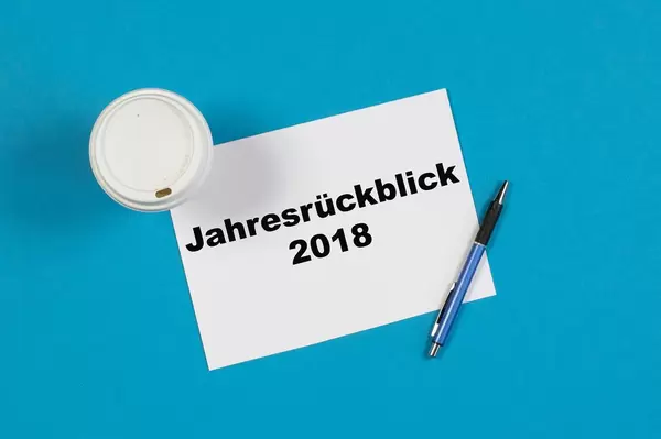 Jahresrückblick 2018 steht auf einem Blatt Papier geschrieben mit Stift und einem Becher Kaffee auf blauem Hintergrund