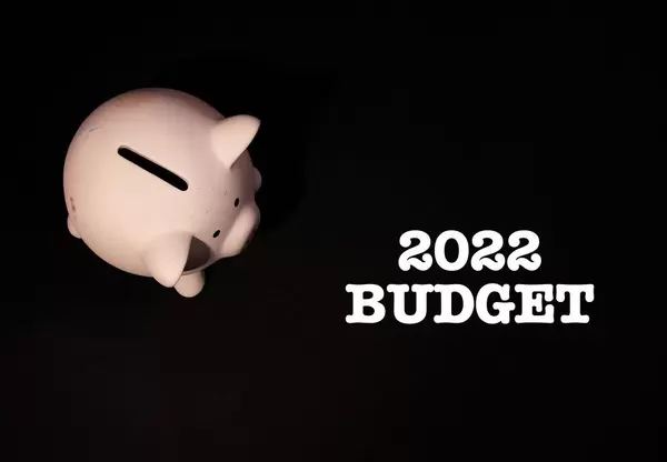 Jahreszahl 2022 mit Aufschrift "Budget", auf schwarzem Hintergrund, neben einem rosa Sparschwein