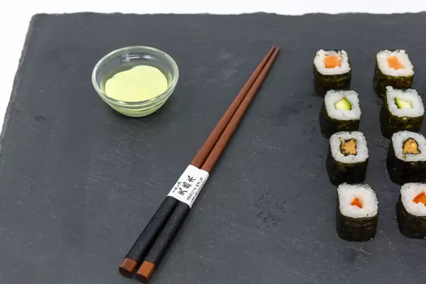Japanische Essstäbchen mit Sushi und Wasabi auf schwarzer Schieferplatte