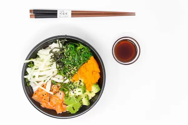 Japanische Küche - Poke Bowl Lachs Teriyaki - mit Sushireis, Lachs, Avocado, Krautsalat, Wakame Salat, Wasago, Nori, Teriyaki-Sauce, Soja-Sauce, Sesam und Schnittlauch