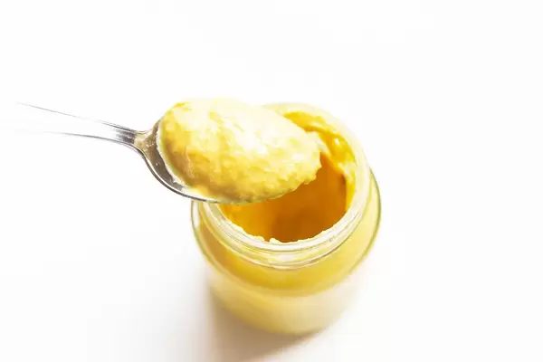 Jar of mustard with spoon on white background