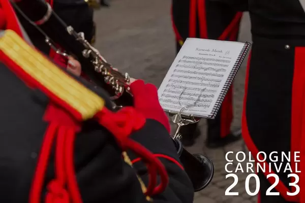 Jecke im Spielmannszug mit Uniform, spielt während des Rosenmontagszug die Klarinette, mit angebrachtem Notenblatt, neben dem Bildtitel "Cologne Carnival 2023" - Kölner Karneval 2023