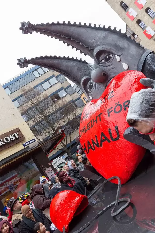 Jecken beim Kölner Rosenmontagszug gedenken der Opfer rechten Terrors: weinender Dom hält ein Herz mit der Aufschrift "Uns Hätz schleiht för Hanau"