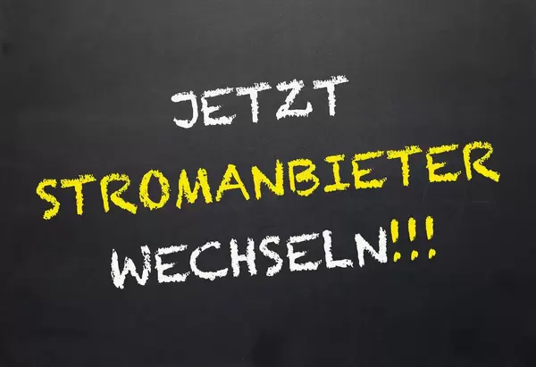 'Jetzt Stromanbieter wechseln!'-Schriftzug mit weißer und gelber Kreide gezeichnet auf Tafel-Untergrund - Nahaufnahme