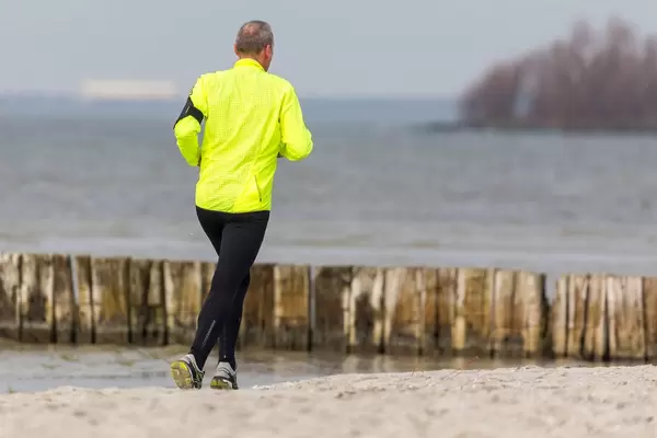 Joggender Mann mit gelber Trainingsjacke am Strand, mit dem Süßwassersee IJsselmeer bei Makkum im Hintergrund