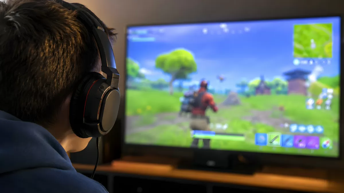 Jugendlicher spielt Fortnite mit Headset am Monitor