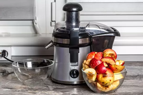 Juice extractor and sliced freshly squeezed apple on kitchen table