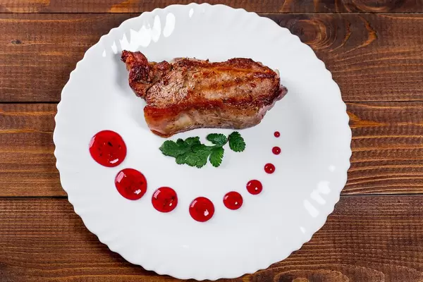 Juicy grilled meat with red sauce on a plate. Top view