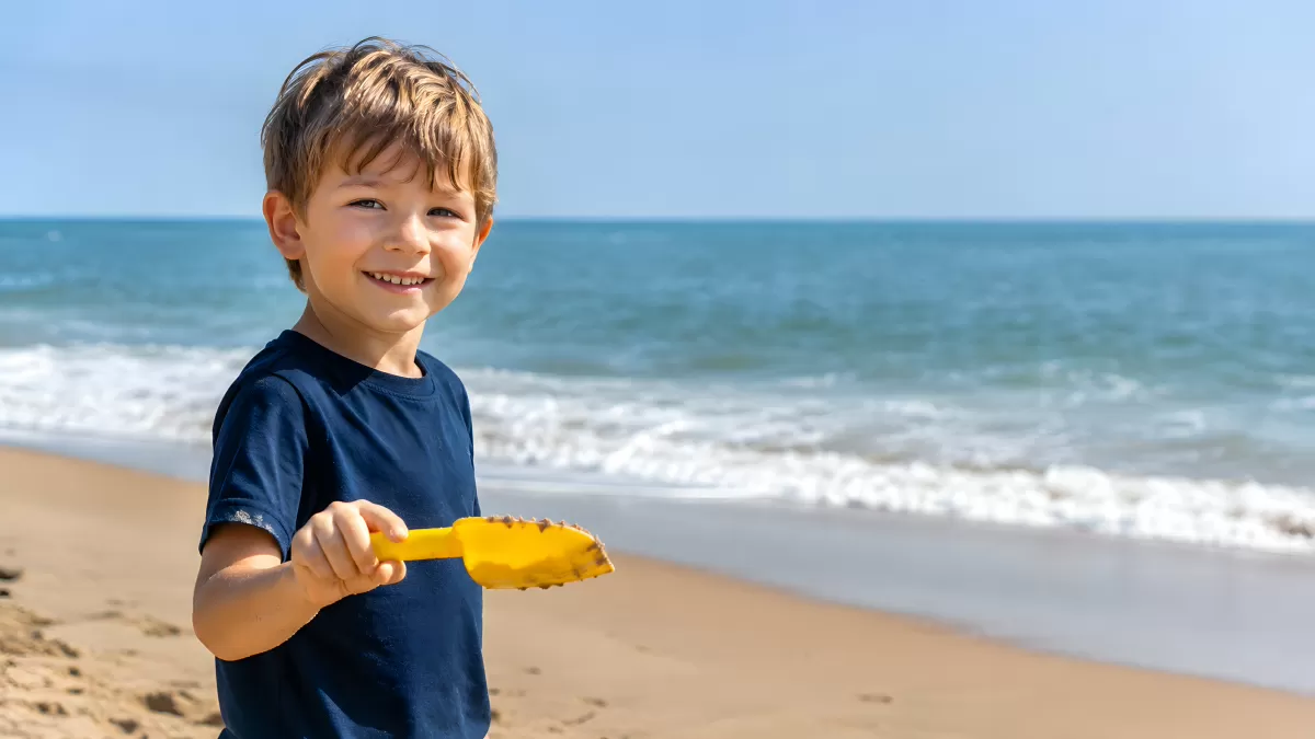 Junge am Strand hält gelbe Schaufel im Sommer