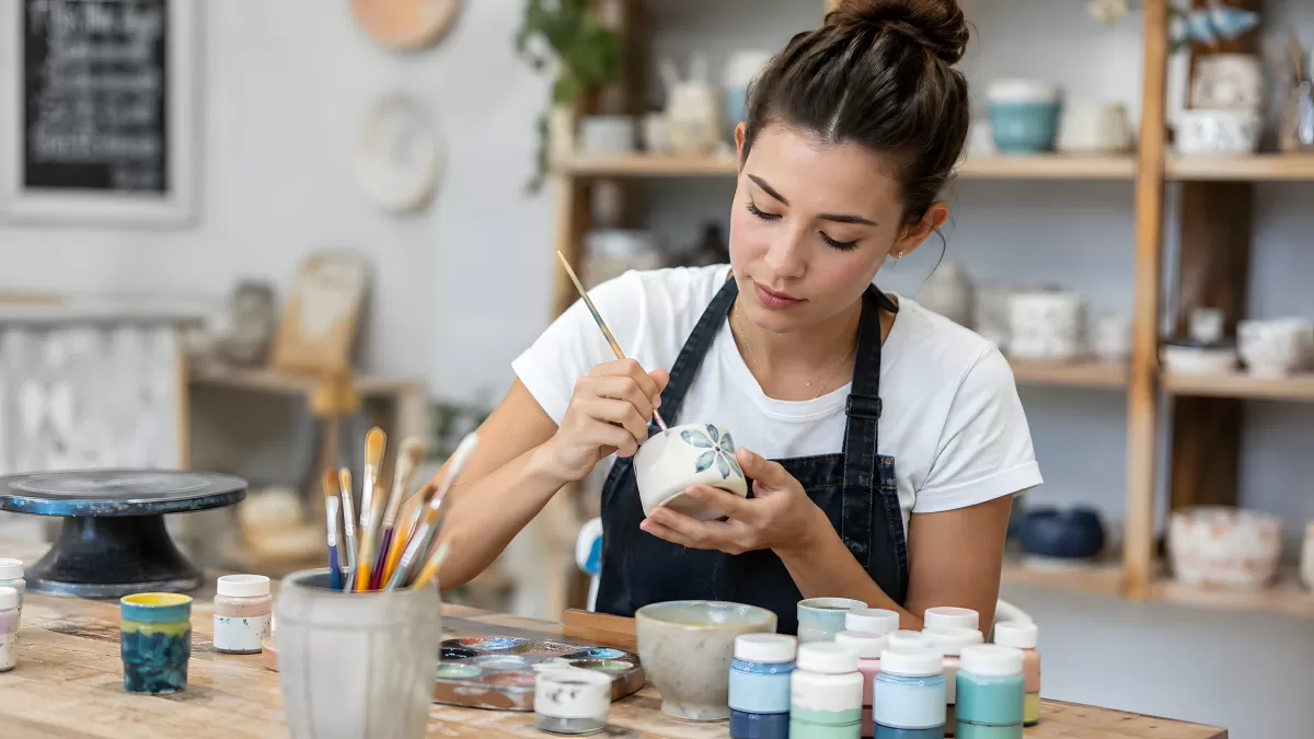 Junge Frau bemalt handgefertigten Keramiktopf im Atelier