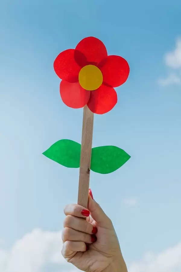Junge Frau hält eine rote Papierblume in der Hand